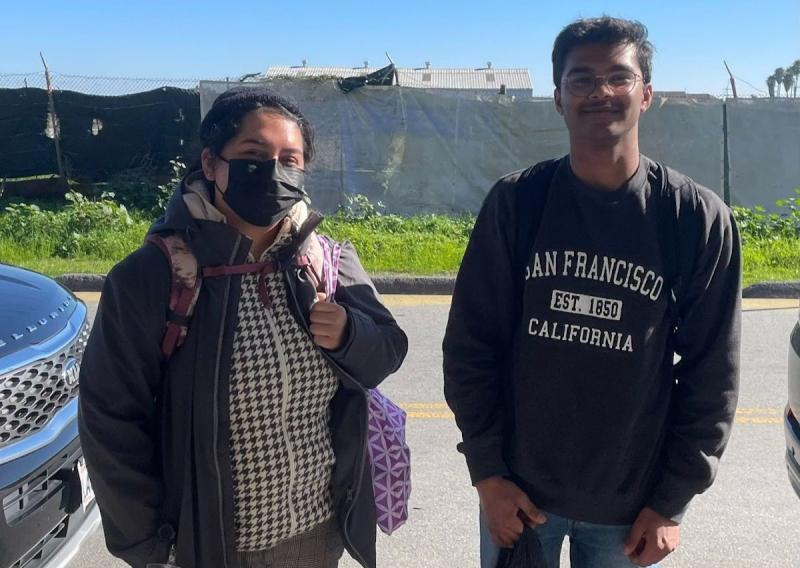 AmeriCorps members Melanie Lopez (left) and Shreyas (right) stand in the center of the frame, facing the camera and smiling. 
